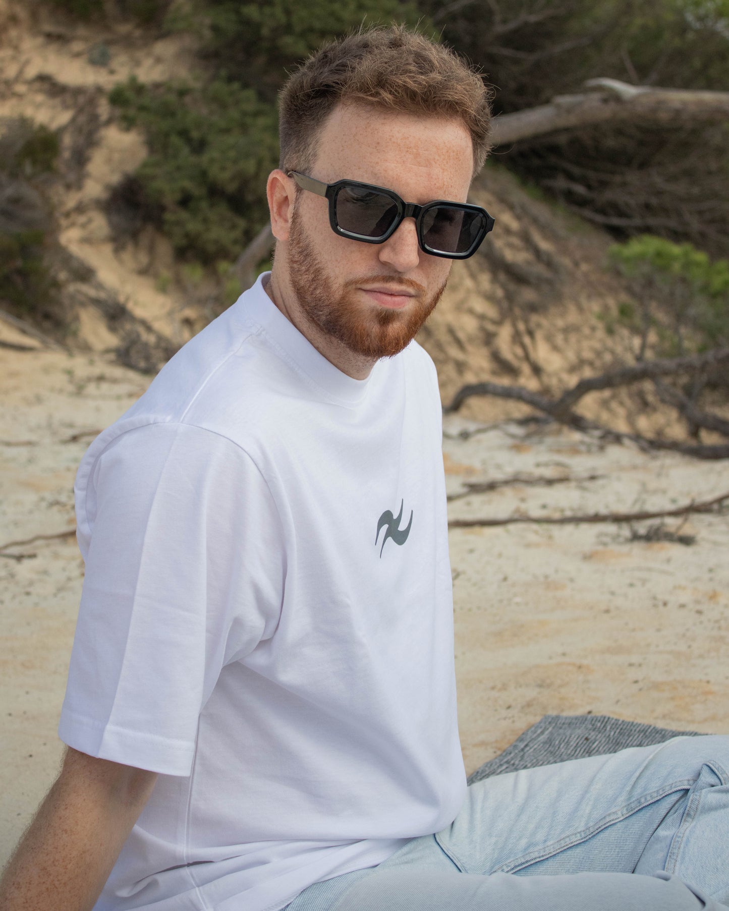 White tee contextualizada en la playa con complementos e icono de la marca